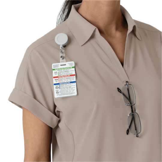 Beige short-sleeve scrub top with open collar, clipped ID badge, and eyeglasses hanging from the front