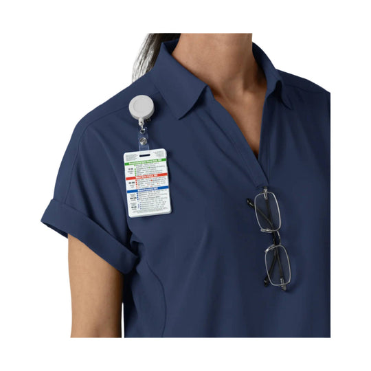 Navy short-sleeve scrub top with clipped ID badge, lanyard, and eyeglasses