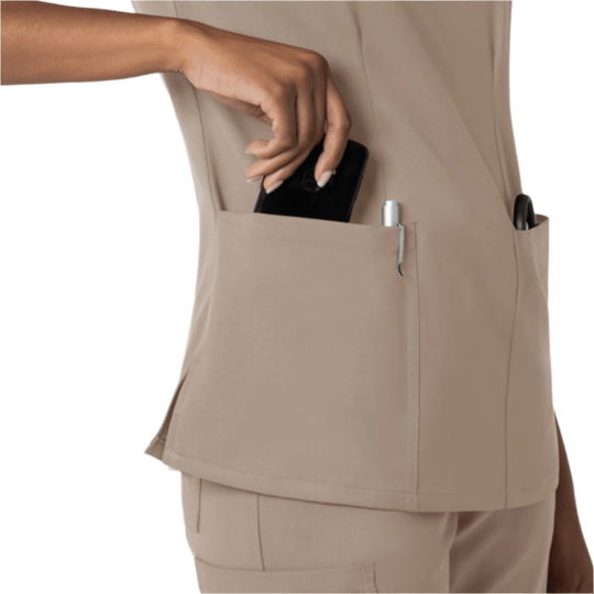 Beige scrub top with side pockets, shown from the side with a phone and pen in the pockets