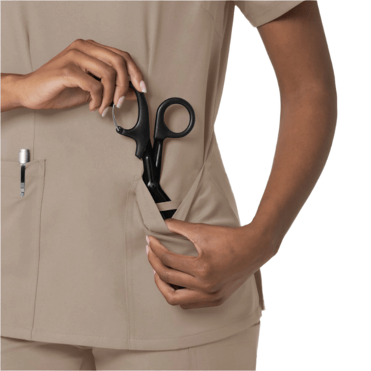Beige scrub top with three pockets, shown with hands pulling open the side pocket