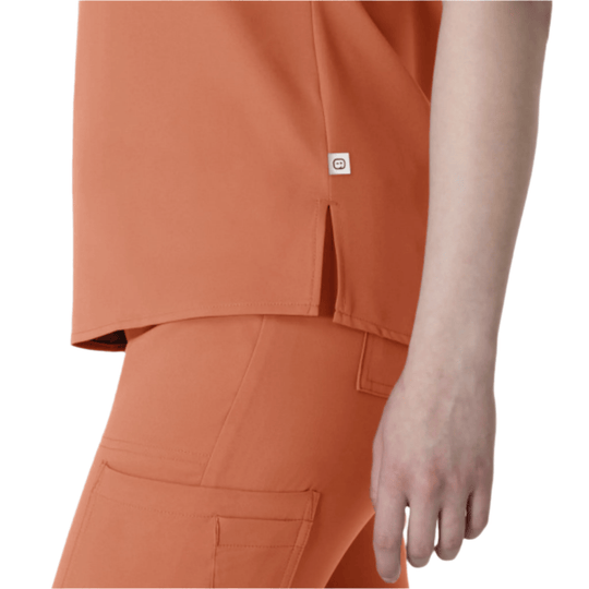 Coral scrub top with side slit and small logo tag, shown with matching pants