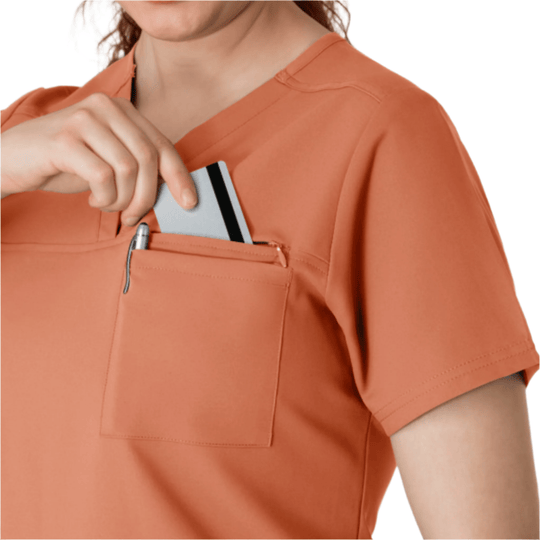Coral short-sleeve V-neck scrub top with a chest pocket and pen slot, shown with a card partially tucked in the pocket