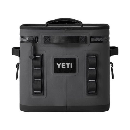 A YETI insulated cooler bag in dark gray with black accents, featuring a top handle, side straps, and a prominent black YETI logo patch on the front, set against a plain white background.