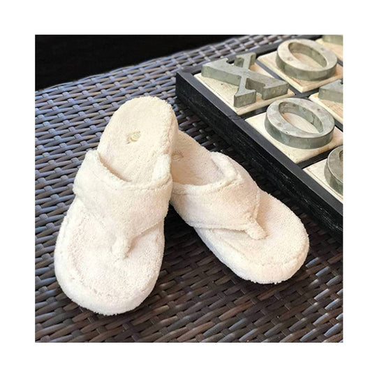 Cream fuzzy thong slippers on a woven surface beside decorative letters