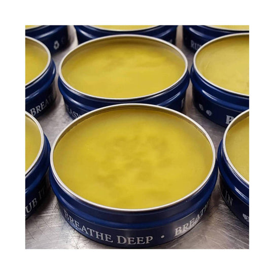 Open blue tins filled with yellow balm, with visible text reading “BREATHE DEEP” on the side