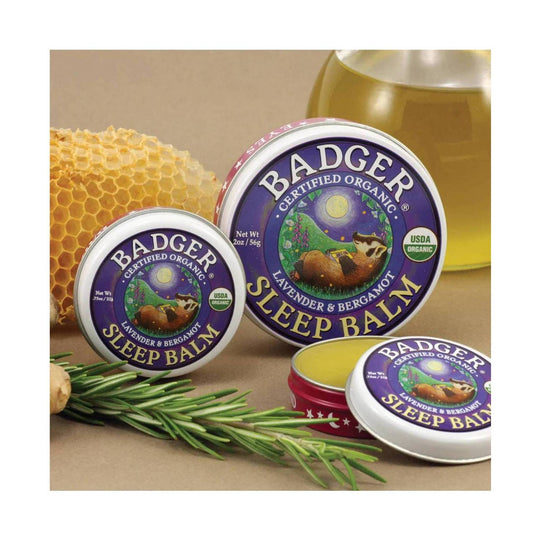 Purple and white round tins of sleep balm with lavender and bergamot labeling, shown with honeycomb and herbs
