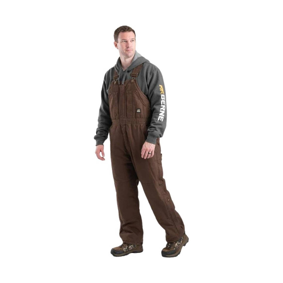 Brown insulated bib overalls worn over a gray hoodie, with BERNE text on the sleeve