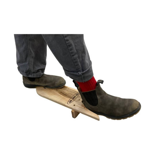 Brown slip-on boots on a wooden balance board, with one red sock visible