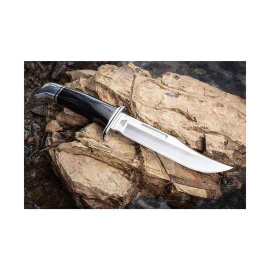 Black-handled hunting knife with a silver fixed blade resting on rocks