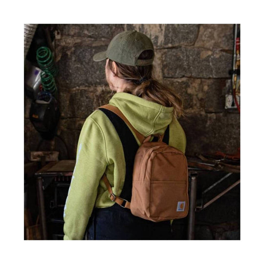 Tan mini backpack worn on the back over a lime green hoodie and olive cap, shown from behind
