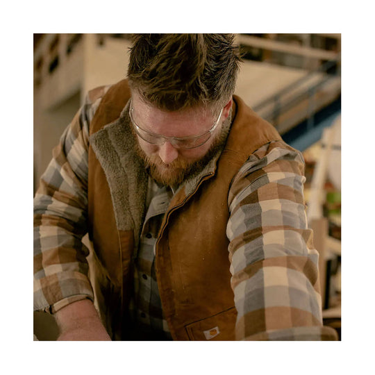 Brown sherpa-lined duck vest over a plaid flannel shirt