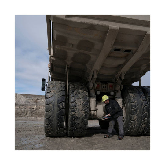 Worker inspecting the underside of a large mining dump truck
