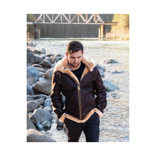 Brown shearling-lined bomber jacket with hood, front zipper, and beige trim worn over a black shirt