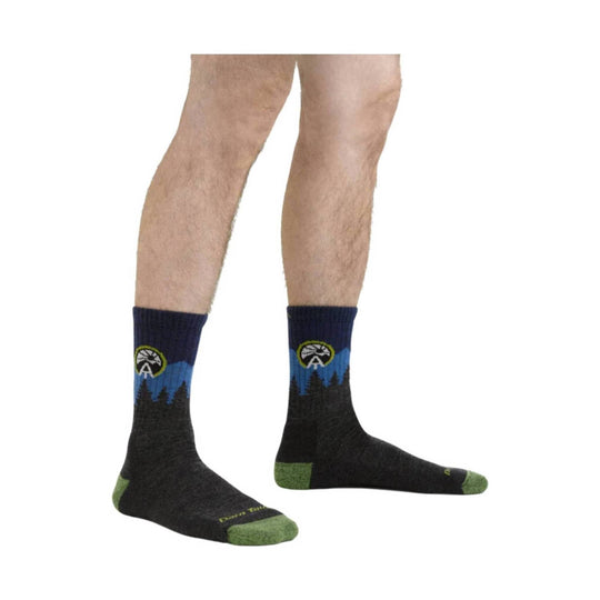 Black crew hiking socks with blue mountain-and-tree pattern and green heels and toes, worn on a model