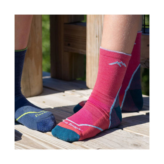 Pink and navy crew hiking socks on children’s feet with small logo text.