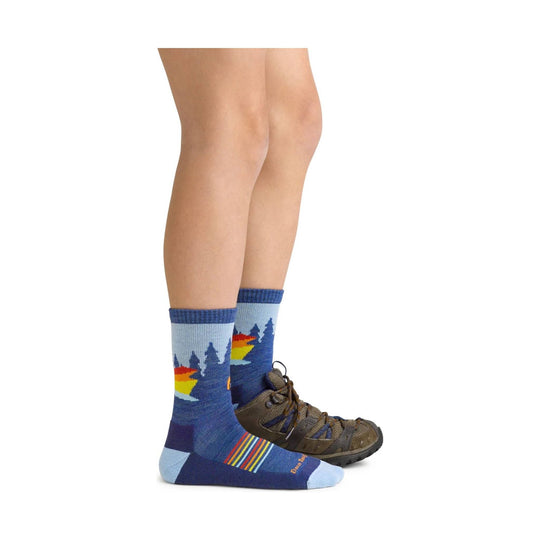 Blue hiking socks with a rainbow stripe and forest silhouette, shown with hiking shoes on a child’s legs