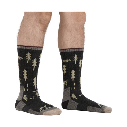Black crew hiking socks with tan tree and bear pattern, shown on lower legs and feet.