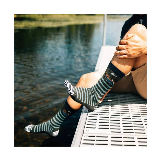 Striped mid-calf socks with black toes and heels worn by someone sitting by the water