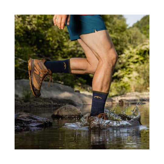 Brown and orange trail hiking shoes worn with navy socks, splashing through a stream