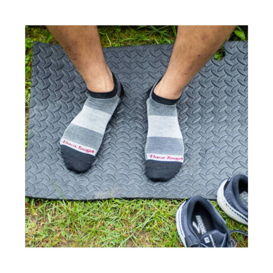Pair of low-cut gray running socks with black toes and heels, worn on feet, with Darn Tough text at the toes