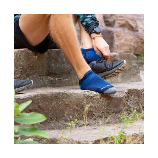 Blue no-show running sock with a gray toe, worn with trail shoes on outdoor stone steps