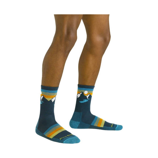 Pair of teal and navy crew socks with mountain and sunset pattern, shown on lower legs and feet