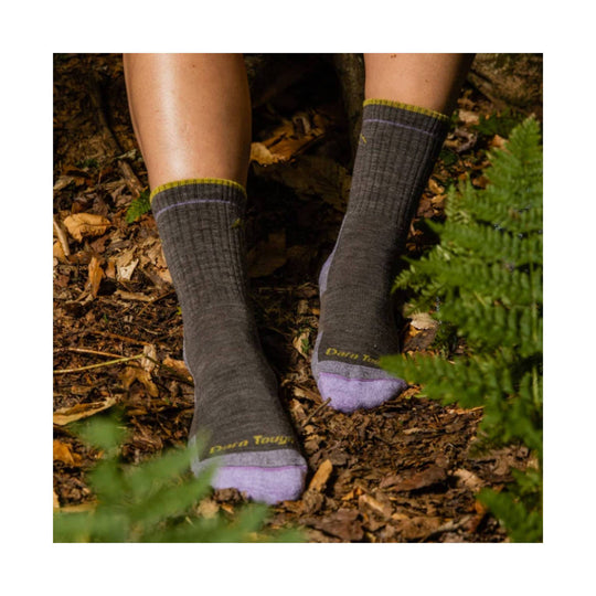 Pair of dark gray hiking socks with lavender toes and yellow trim, shown on legs in a forest setting