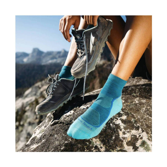 Turquoise ankle hiking sock worn with trail shoes on a rocky ledge