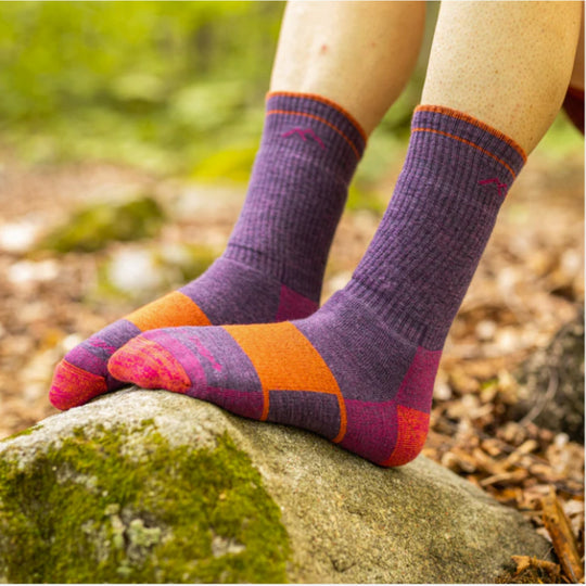 Purple and orange patterned crew hiking socks on a person's feet resting on a mossy rock