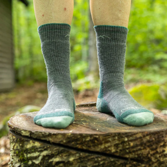 Pair of gray and teal ribbed hiking socks worn outdoors on a tree stump