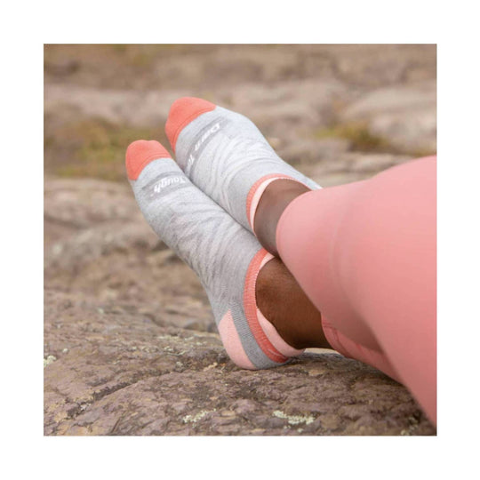 Light gray no-show running socks with coral toes and heels worn with pink leggings on a rocky surface.