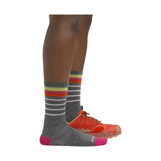 Gray crew socks with white stripes, rainbow bands, and pink toe and heel on a model wearing bright orange shoes.