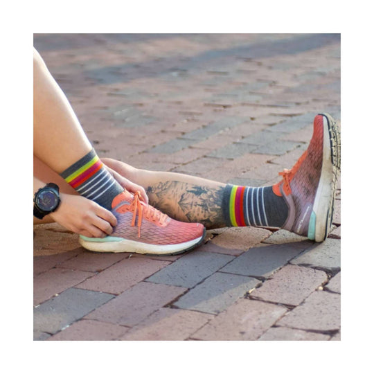 Gray low-cut running sock with multicolor striped cuff worn with coral running shoes
