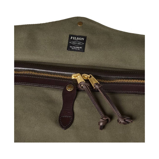 Olive canvas duffle bag with brown leather trim, brass zipper, and hanging leather zipper pulls