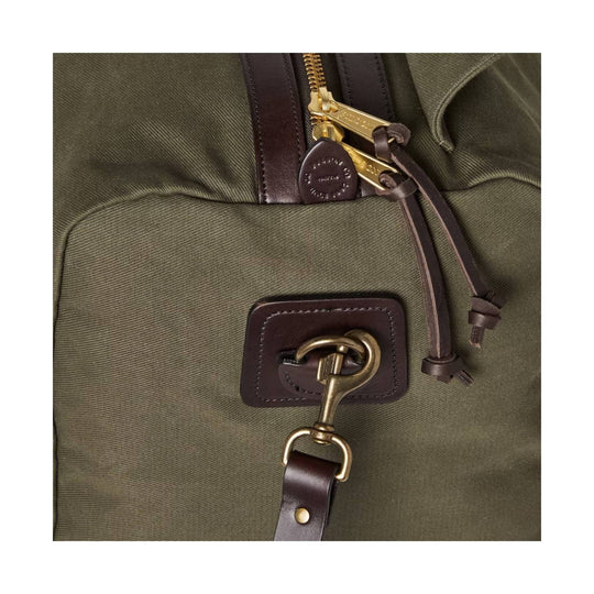 Olive canvas duffle bag with brown leather trim, brass zipper, and front D-ring