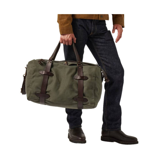 Olive canvas duffel bag with brown leather handles and straps, shown beside a man holding it