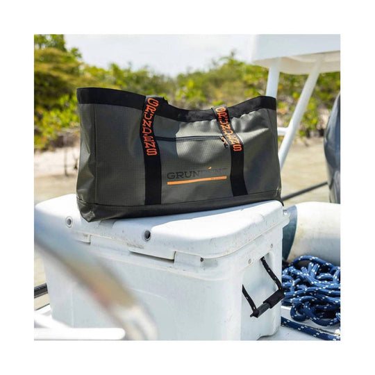 Black tote bag with orange GRUNDENS straps and front zipper pocket, shown on a boat deck