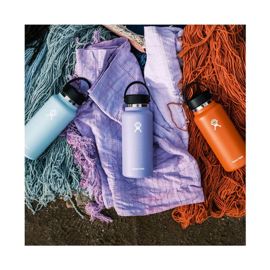 Three matte insulated water bottles in pastel blue, lavender, and orange on textured blankets