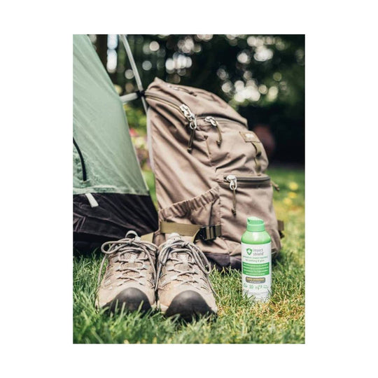 Green bottle of insect repellent beside hiking boots and a backpack at a campsite