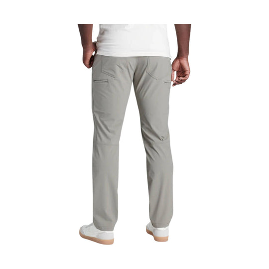 Light gray men’s cargo pants shown from the back, with zippered thigh pockets and white sneakers