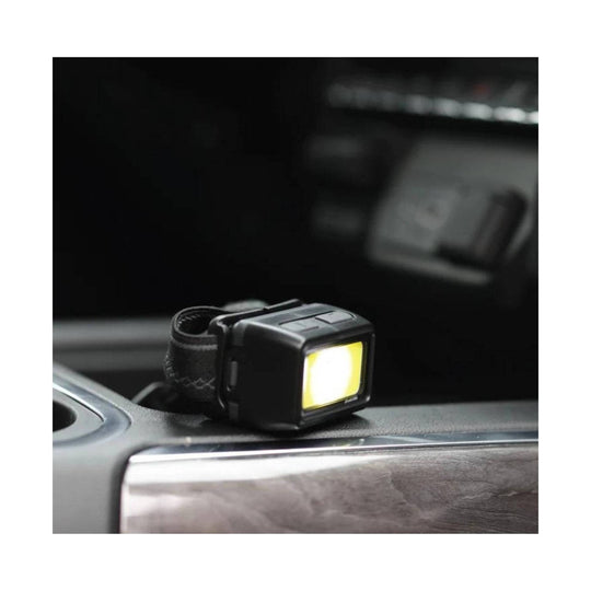 Black headlamp with strap, lit yellow front panel, resting on a car dashboard.