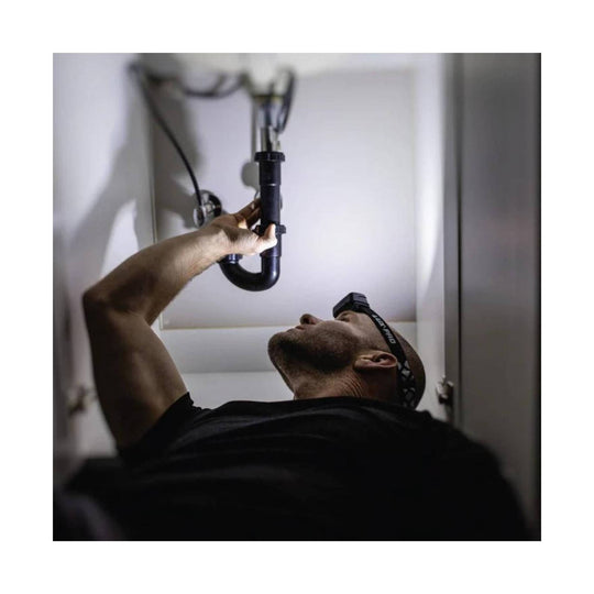 Black headlamp with adjustable head strap worn while inspecting plumbing under a sink
