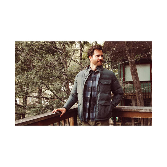 Dark gray quilted down jacket worn over a blue plaid shirt, shown on a man standing outdoors