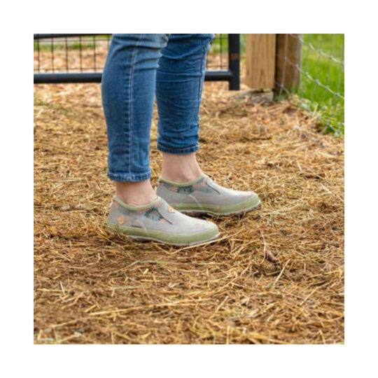 Light gray slip-on rain shoes with floral side panels and green soles, worn with blue jeans.