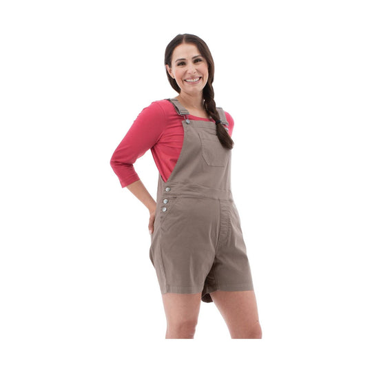 Woman wearing taupe overall shorts over a pink long-sleeve shirt, standing against a white background