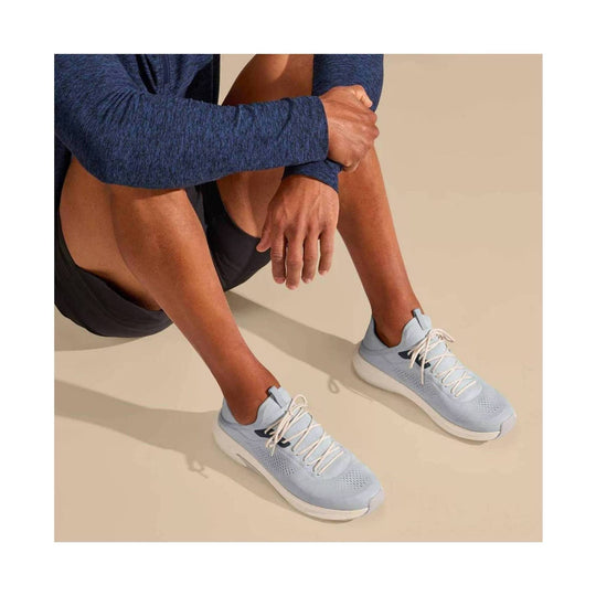 Light blue athletic shoes with white soles and laces worn by a seated model