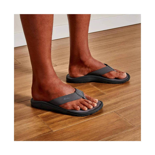 Gray thong sandals with black textured soles on feet indoors