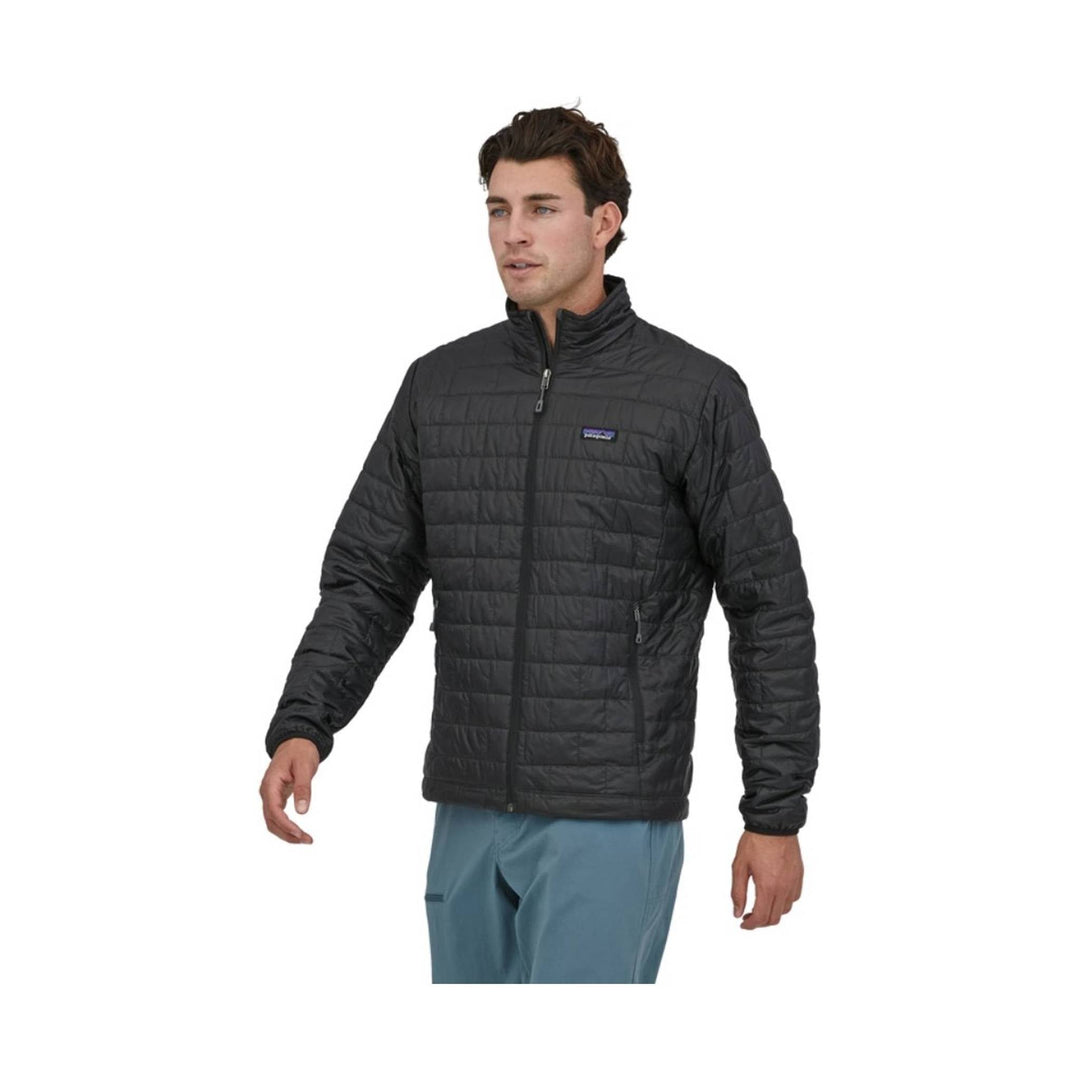 Black quilted zip-up jacket with a stand collar and chest logo patch, worn by a model