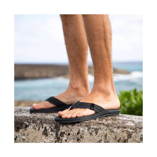 Black thong sandals worn on a rocky ledge with an ocean backdrop