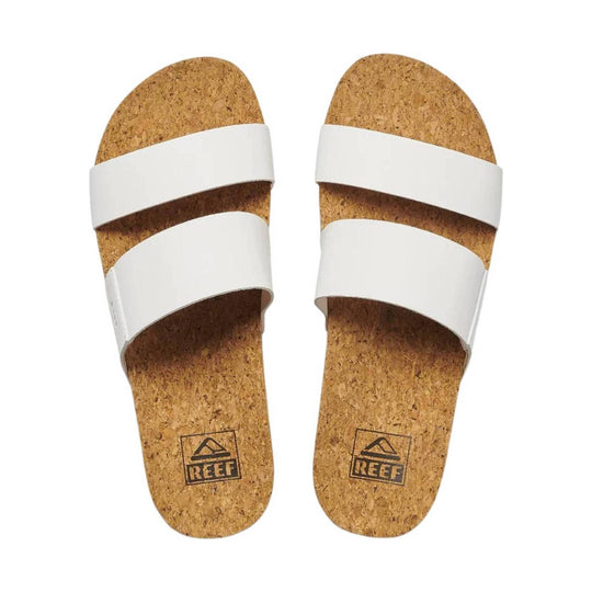 White double-strap slide sandals with cork footbeds and REEF logos